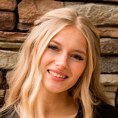 Person with long, wavy blonde hair standing in front of a textured stone wall