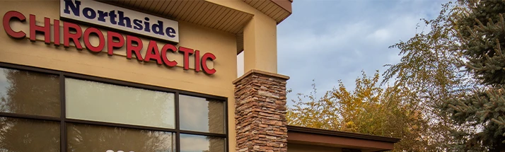 Exterior view of a building with the sign 'Northside Chiropractic' in bold letters, featuring beige walls, large windows, and a stone column